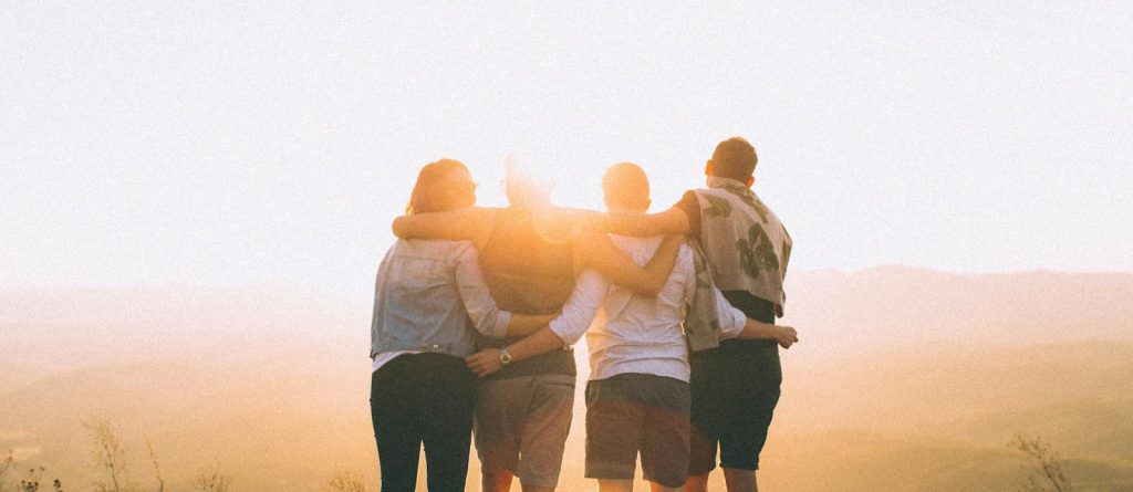 Four Person Standing on Cliff in Front of Sun