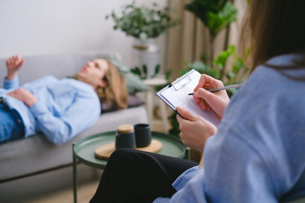 Crop psychotherapist taking notes during psychotherapy session with patient