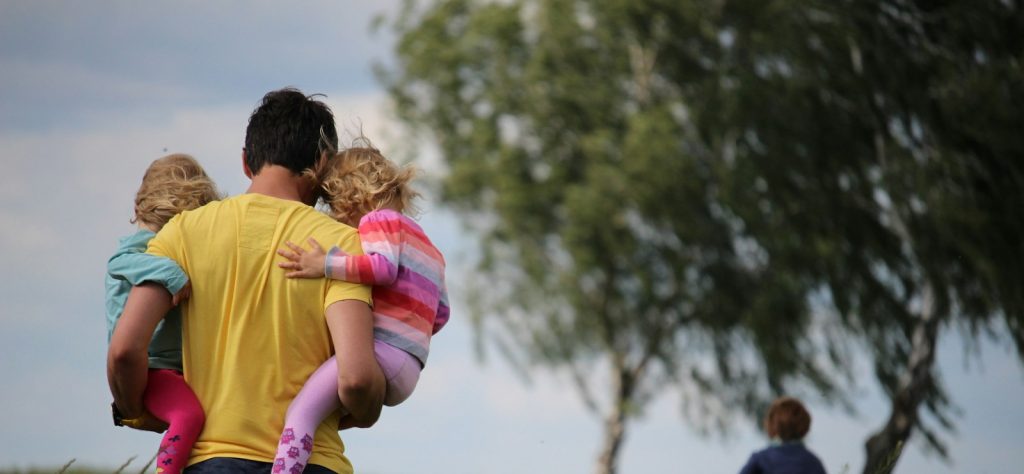 man carrying to girls on field of red petaled flower